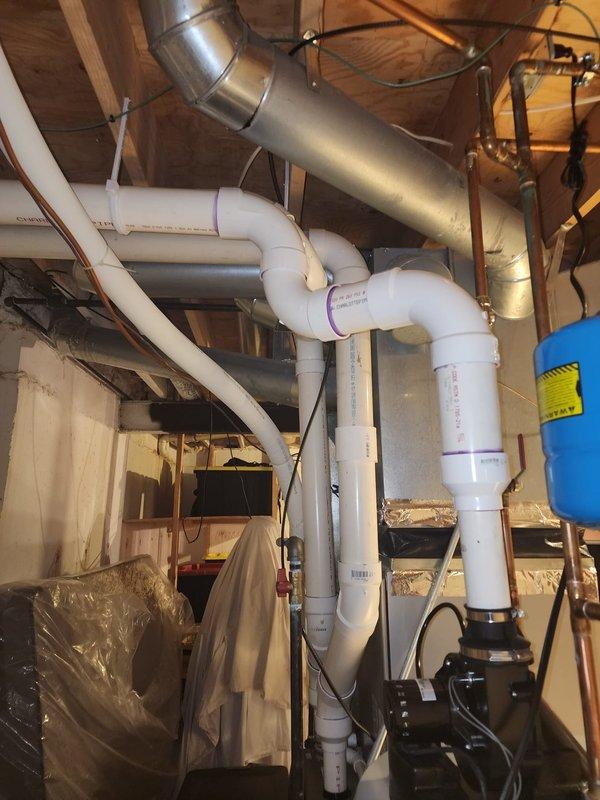 Responded to warranty call for water heater venting inspection. Upon arrival, identified cellular core PVC piping installed as water heater exhaust venting system, which does not meet manufacturer specifications or code requirements for proper combustion gas venting. Documented existing installation showing white PVC vent piping running vertically and horizontally through basement utility area with multiple bends and connections. Photographed complete venting configuration including connections to water heater unit, routing through ceiling joists, and relationship to surrounding HVAC ductwork and plumbing systems. Advised that approved venting materials per installation manual must be used, typically Category III stainless steel or approved polypropylene/CPVC rated for water heater flue gases. Completed required photographic documentation and follow-up form for warranty review and corrective action planning.