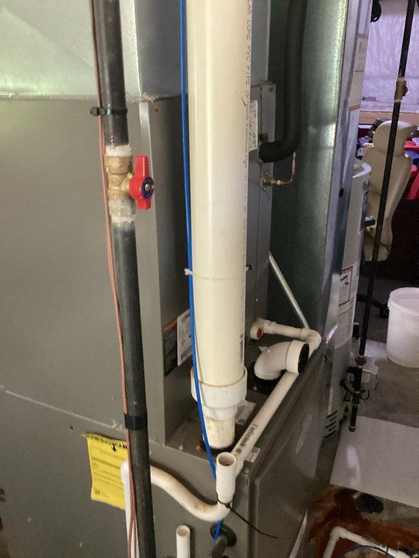 Conducted comprehensive furnace replacement estimate for residential HVAC system with failed heat exchanger. Documented existing gray metal air handler installation showing significant water damage on surrounding concrete floor with rust-colored staining, indicating previous moisture intrusion or condensate drainage issues. Photographed complete system configuration including white PVC condensate piping, blue wiring, electrical control panel with yellow manufacturer label, green cylindrical air handler unit, and associated plumbing connections with red valve handle on gray supply lines. Assessed mechanical room conditions and equipment accessibility for replacement procedures.