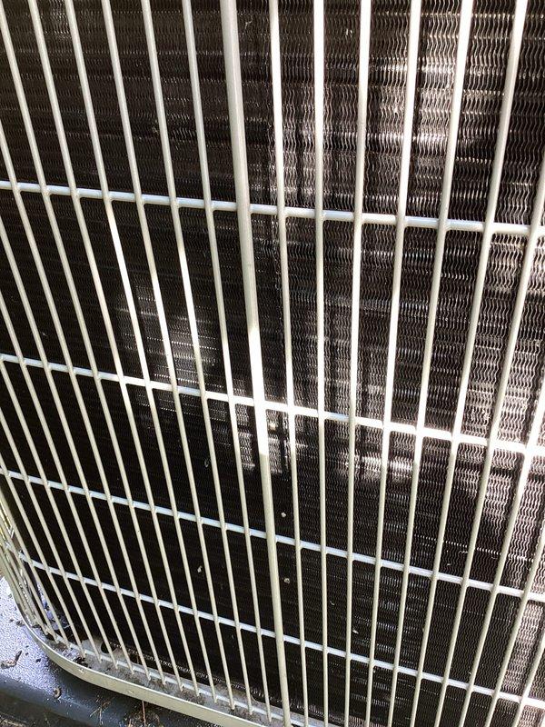 Responded to service call for intermittent buzzing noise and inadequate cooling from air conditioning system. Upon arrival, performed visual inspection of outdoor condenser unit, examining protective grille, condenser coil fins, fan assembly, compressor, refrigerant lines, and electrical connections. Documented equipment condition with photographs showing normal wear consistent with outdoor exposure and minor accumulation of dirt and debris on internal components and base plate.