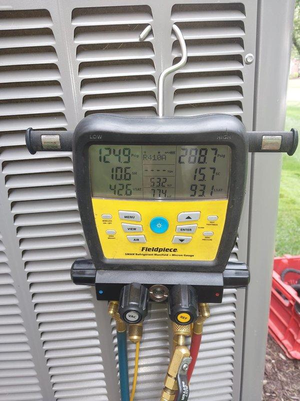 Responded to service call for condensation in basement with ice buildup on air conditioning unit. Upon arrival, confirmed evaporator coil had experienced freezing condition. Advised customer to allow unit to completely thaw before system restart. Utilized Fieldpiece SMAN refrigerant manifold with micron gauge to assess system pressures and performance. Measured refrigerant pressures showing LOW side reading of 124.9 PSI and HIGH side reading of 208.7 PSI for R410A refrigerant system. Inspected evaporator coil assembly and copper refrigerant lines within ductwork, checking for proper connections and electrical wiring integrity. Documented system conditions with photographic evidence showing gauge readings and internal coil access panel. Confirmed multi-colored control wiring and copper tubing configuration were properly secured with cable management. Scheduled follow-up assessment after thaw period to determine root cause of freezing condition, which may include restricted airflow, low 