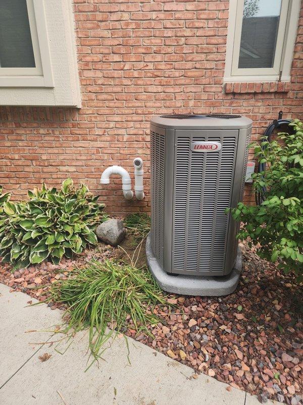 Completed installation of Lennox 4-ton variable speed condenser unit as warranty replacement. Unit positioned on concrete pad against exterior brick wall with proper clearances, connected to existing refrigerant lines and electrical disconnect. Removed and returned original condenser to shop per company protocol.