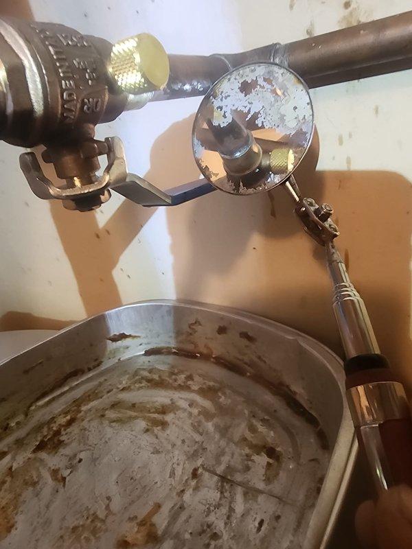 Responded to water leak at tanked water heater installation. Upon inspection, identified active leak at soldered connection on 1/2-inch ball valve with bleeder drain. The copper piping system showed signs of age and weathering, with visible corrosion and patina on connections. Repaired faulty solder joint at valve connection point, ensuring proper seal and eliminating leak. Inspected drain pan beneath water heater, which showed evidence of previous water accumulation and rust staining. Tested all connections for integrity after repair and verified system was operating without leaks.