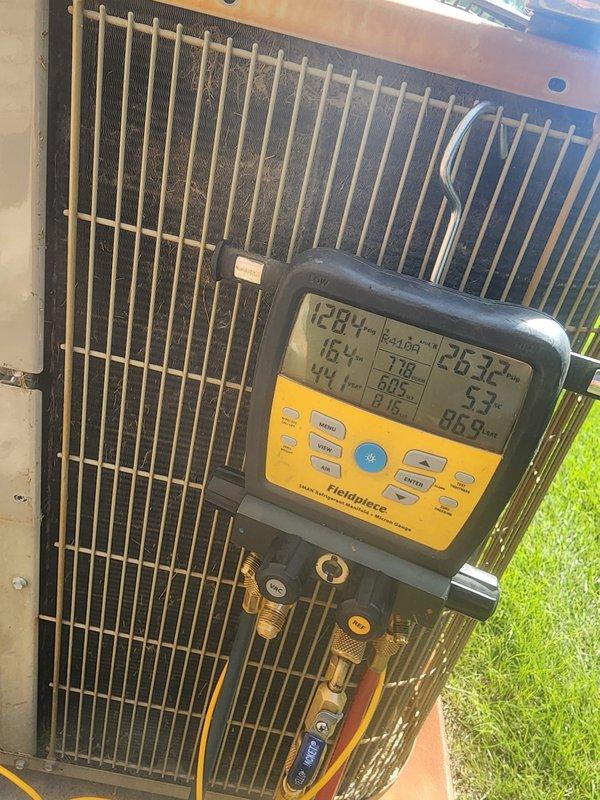 Performed comprehensive cooling season maintenance on outdoor air conditioning unit. Connected diagnostic gauges and measured system pressures and temperatures, with readings indicating 203.7 PSI high side, 86.9 PSI low side, and temperatures of 128.4°F discharge, 44°F suction, with 16.4°F superheat. Inspected condenser coil fins for debris accumulation, verified fan motor operation and fan guard security, and examined electrical components including capacitor and wiring connections. All system parameters found within normal operating range, unit operating efficiently with no deficiencies noted.
