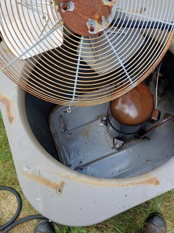 Completed routine AC maintenance on outdoor condensing unit showing significant age and weathering. Performed standard tune-up procedures including inspection of compressor, fan motor, and electrical components; all major components found operational despite visible exterior corrosion on housing and top plate. Cleaned condenser coil fins, checked refrigerant lines, verified proper drainage function, and documented equipment condition with extensive rust present on metal surfaces from prolonged outdoor exposure.