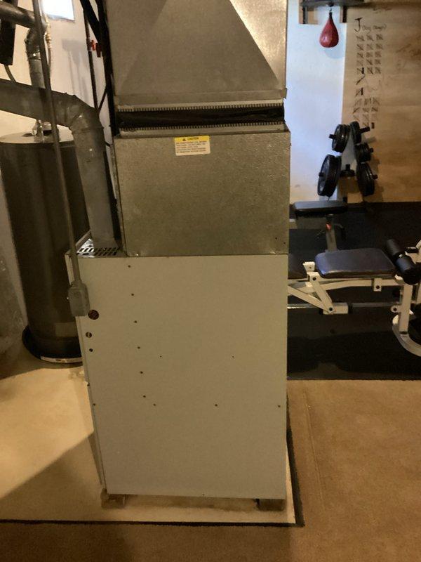 Performed site evaluation for 27-year-old residential air conditioning system replacement. The existing outdoor condensing unit showed signs of age-related failure and was no longer operational. Documented current equipment configuration including outdoor condenser unit positioned on concrete pad with decorative rock landscaping, refrigerant line set routing through black flexible conduit, and indoor air handler/furnace system located in basement utility area. Photographed existing installation showing proper clearances, electrical connections, and ductwork connections to facilitate accurate equipment sizing and replacement planning for new HVAC system installation.