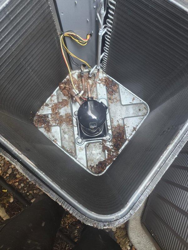 Responded to callback for thermostat temperature control issue where unit would not lower temperature from 1-5 degrees. Upon arrival, inspected outdoor condenser unit and found heavy dirt and grime accumulation on exterior surfaces and fins, along with significant rust and corrosion on compressor mounting plate. Documented equipment condition showing environmental deterioration and debris buildup that could impact system performance and airflow efficiency. Verified refrigerant line connections and compressor operation during inspection.