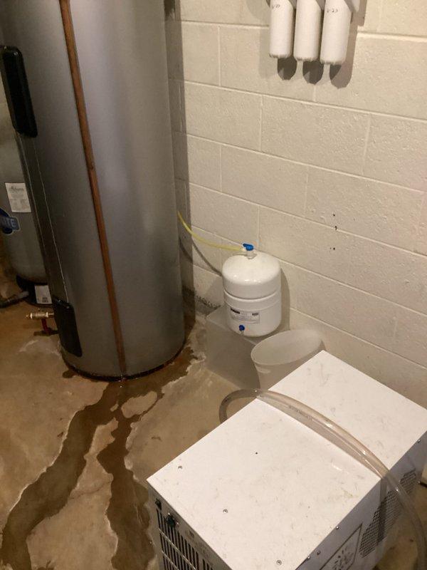 Conducted on-site assessment for water heater replacement in basement of residential property constructed in 1969. Upon arrival, discovered active water leak from existing water heater with significant water pooling on concrete floor around base of unit and spreading to surrounding equipment. Documented failed water heater with metallic silver exterior, undetermined age, installed against painted cinderblock wall with expansion tank, copper piping, flexible connectors, and PVC venting system. Photographed leak damage, standing water affecting floor area, and complete installation configuration including all connections, pressure relief valve, shut-off valves, and electrical wiring for replacement planning purposes. Provided estimate for complete water heater replacement including removal of failed unit and installation of new system.