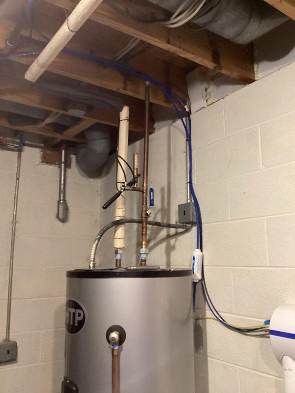 Conducted on-site assessment for water heater replacement in basement of residential property constructed in 1969. Upon arrival, discovered active water leak from existing water heater with significant water pooling on concrete floor around base of unit and spreading to surrounding equipment. Documented failed water heater with metallic silver exterior, undetermined age, installed against painted cinderblock wall with expansion tank, copper piping, flexible connectors, and PVC venting system. Photographed leak damage, standing water affecting floor area, and complete installation configuration including all connections, pressure relief valve, shut-off valves, and electrical wiring for replacement planning purposes. Provided estimate for complete water heater replacement including removal of failed unit and installation of new system.