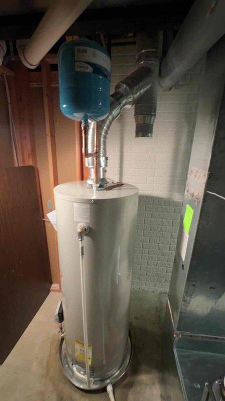 Successfully installed a new 50-gallon residential tanked water heater in the basement utility area, complete with proper copper piping connections and a blue expansion tank mounted above the unit. All plumbing connections were secured to code specifications, with the water heater positioned on the concrete floor against the foundation wall for optimal access and safety clearance. The installation included integration with existing HVAC systems in the mechanical room, ensuring proper ventilation and operational efficiency.