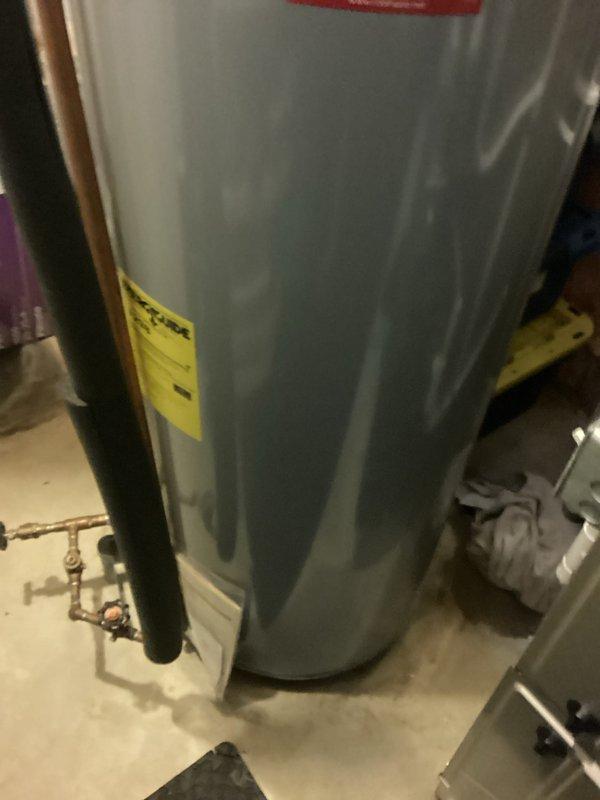 Completed water heater estimate for residential installation in basement mechanical room. Assessed existing water heater unit with copper piping connections, shut-off valves, and proper venting configuration. Documented current equipment specifications, plumbing connections, and installation conditions including exposed wall framing with fiberglass insulation. Photographed water heater unit showing manufacturer labeling, piping layout with brass fittings, red-handled valves, and proximity to existing HVAC equipment. Evaluated mechanical room accessibility and clearances for potential replacement installation.