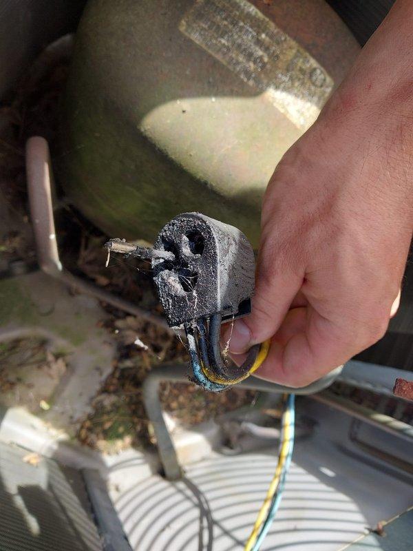 Responded to no cooling complaint on air conditioning system. Upon inspection, discovered severely corroded and burned electrical connector at compressor motor, indicating electrical failure and potential motor seizure. The connector exhibited significant heat damage with charred material and deteriorated housing, confirming loss of electrical continuity to the compressor. Documented equipment condition with photos showing the failed connector and compressor unit with visible age-related deterioration. System requires replacement of damaged electrical components and further diagnostic testing to determine compressor motor viability before restoration of cooling operation.