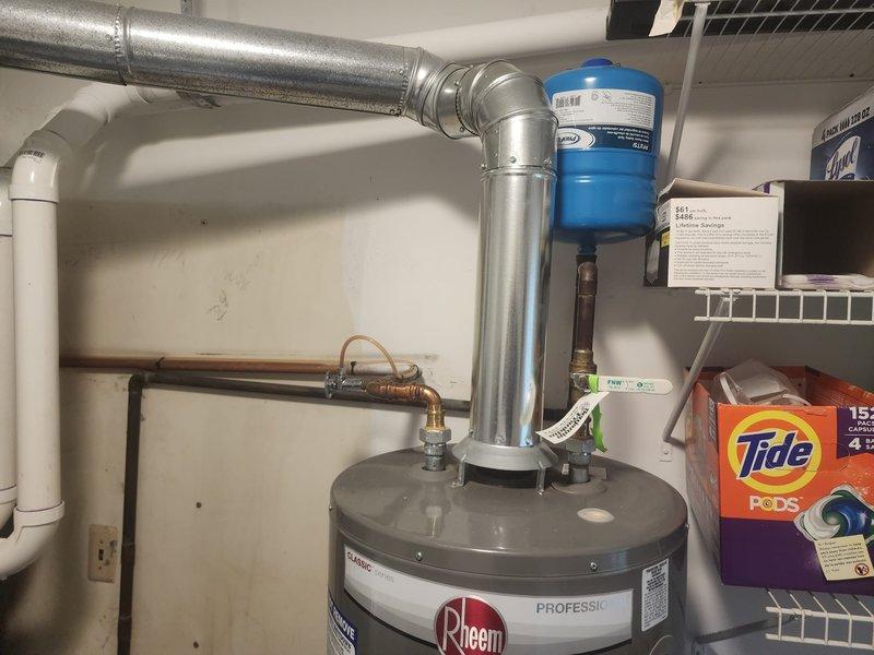 Responded to service call for reported water heater leak. Upon arrival, performed thorough inspection of Rheem Professional series tanked water heater unit and surrounding plumbing connections. Examined all visible components including copper supply lines, brass fittings, temperature and pressure relief valve, drain valve, and tank exterior for signs of moisture or active leaking. Inspected overhead ductwork connections and exhaust vent pipe for proper installation and clearances. Documented equipment condition with photographs showing water heater installation, blue water treatment filter system, and associated mechanical room plumbing infrastructure. Verified warranty status and provided assessment findings for next steps.