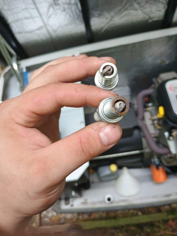 Performed scheduled maintenance on residential standby generator unit. Removed and inspected spark plugs, finding carbon buildup on one plug indicating normal combustion deposits from operation. Replaced spark plugs with new units to ensure reliable ignition and optimal engine performance. Completed oil change service, draining used oil into collection pan and refilling with fresh oil to manufacturer specifications. Verified all internal components, including air filter assembly, electrical connections, and control panel wiring for proper operation. Closed and secured cabinet panels upon completion of maintenance tasks.