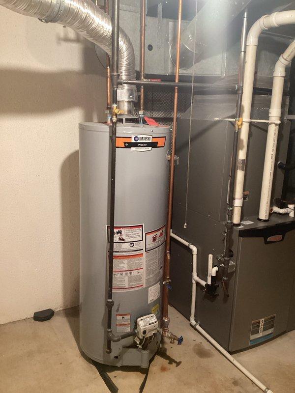 Completed comprehensive estimate for water heater replacement in residential basement mechanical room. Assessed existing tall cylindrical water heater with Trane control device, evaluated copper supply and discharge piping configurations, flexible ductwork connections, and proximity to existing HVAC furnace unit with associated PVC condensate drainage system. Documented current equipment specifications, noted floor staining indicating previous moisture concerns, photographed all mechanical connections including brass fittings and shut-off valves, and provided replacement options for new water heater installation with proper venting and plumbing modifications as required.
