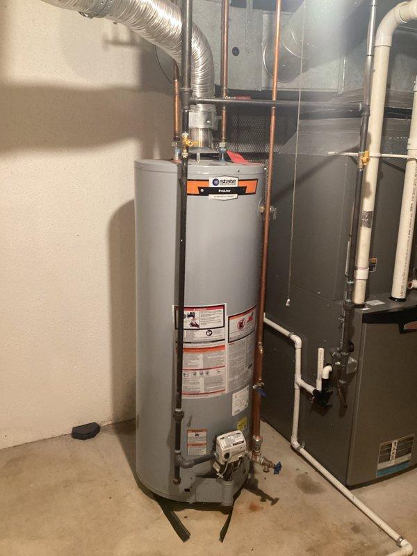 Completed comprehensive estimate for water heater replacement in residential basement mechanical room. Assessed existing tall cylindrical water heater with Trane control device, evaluated copper supply and discharge piping configurations, flexible ductwork connections, and proximity to existing HVAC furnace unit with associated PVC condensate drainage system. Documented current equipment specifications, noted floor staining indicating previous moisture concerns, photographed all mechanical connections including brass fittings and shut-off valves, and provided replacement options for new water heater installation with proper venting and plumbing modifications as required.