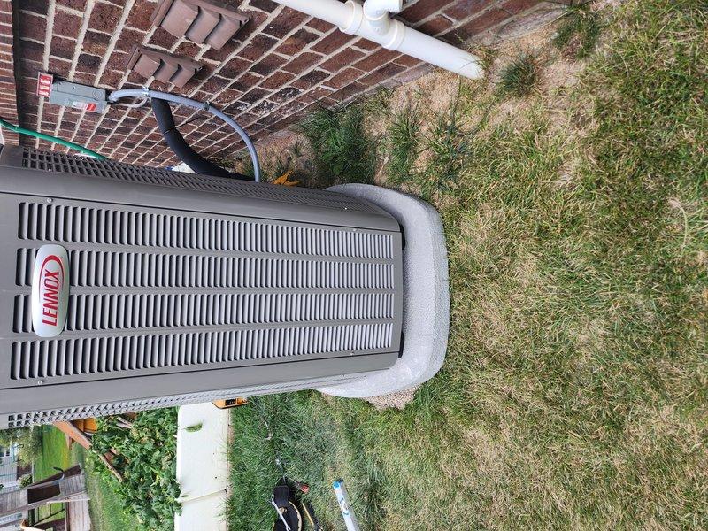 Completed full HVAC system installation including Lennox furnace, air conditioner condenser unit, whole-home humidifier, and S40 smart thermostat. The indoor furnace unit was installed in the mechanical room with proper venting and condensate drainage via white PVC piping, while the outdoor Lennox condenser was positioned on a concrete pad adjacent to the brick foundation with refrigerant lines properly connected and secured.