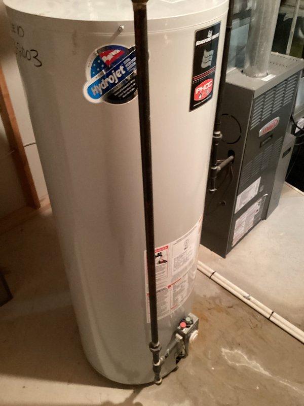 Conducted on-site assessment and provided estimate for water heater replacement in residential basement mechanical room. Evaluated existing white cylindrical tank-style water heater with visible manufacturer specifications and aging components, including copper supply piping with red valve handles. Documented current installation configuration adjacent to gray furnace unit with metallic ductwork in unfinished utility space. Photographed equipment conditions, piping connections, venting arrangements, and clearances to nearby HVAC system for accurate replacement planning and material specifications.