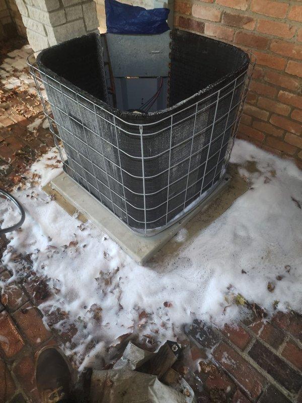 Completed comprehensive tune-up and maintenance on 21-year-old outdoor air conditioning unit located in backyard brick enclosure. Performed standard preventive maintenance procedures including coil cleaning, which generated foam residue visible around unit base on concrete pad. Inspected internal components including evaporator coils, motor assembly, drain pan, and electrical connections; noted age-related discoloration on coil surfaces but system operational. Unit protected by wire cage guard and functioning within normal parameters with no reported issues prior to service.