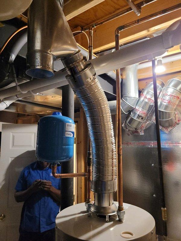 Successfully installed a 40-gallon Bradford White tanked water heater in the basement utility area. The installation included connecting copper supply lines, installing a blue expansion tank with proper piping configuration, and venting the unit with flexible metallic ductwork connected to the existing black metal flue system that extends through the ceiling joists. All connections were secured and tested to ensure proper operation of the new water heating system.