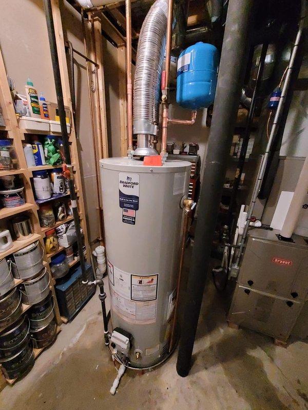 Successfully installed a 40-gallon Bradford White tanked water heater in the basement utility area. The installation included connecting copper supply lines, installing a blue expansion tank with proper piping configuration, and venting the unit with flexible metallic ductwork connected to the existing black metal flue system that extends through the ceiling joists. All connections were secured and tested to ensure proper operation of the new water heating system.