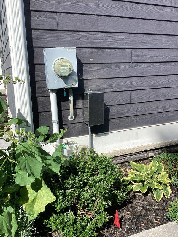 Conducted site assessment for whole house generator installation to replace customer's existing portable generator unit. Evaluated existing electrical service panel, gas meter assembly, and utility infrastructure to determine optimal placement and connection requirements for an 11kW single-phase automatic standby generator system. Documented current gas metering equipment, electrical meter location, and available space on exterior wall with dark gray siding. Identified adequate gas supply line accessibility and confirmed electrical service compatibility for generator integration. Photographed existing utility connections including gas regulator assembly, electrical meter box with PVC conduit, and surrounding landscape features to assess clearance requirements and installation constraints. Prepared comprehensive estimate for generator procurement, transfer switch installation, gas line extension, electrical panel modifications, and automatic transfer system integration to provide seamle