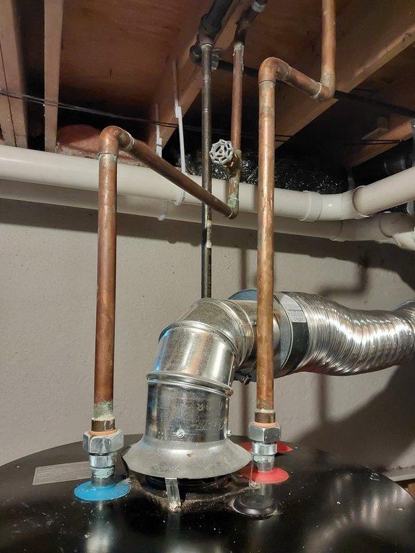 Responded to service call for leaking water heater in basement. Upon inspection, identified active leak originating from pipe connection on Whirlpool tanked water heater unit. Inspected copper supply lines, shut-off valves, and connection points to determine source of leak. Documented existing plumbing configuration including hot and cold water supply lines with compression fittings and shut-off valve. Photographed water heater installation showing supply piping, flexible ductwork for ventilation, and associated mechanical components in utility area. Assessed overall condition of unit and surrounding plumbing infrastructure to provide repair recommendations.