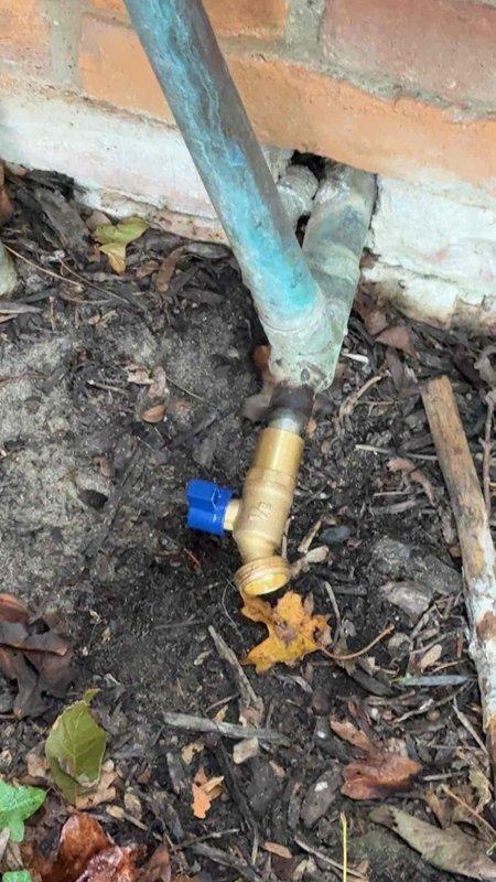 Replaced faulty ball valve on exterior hose bib connection serving garden sprinkler system. The existing brass valve showed significant wear and corrosion, preventing proper water flow control. Installed new brass ball valve with blue handle at foundation-level connection point where galvanized supply line meets PVC distribution pipe. Service completed during scheduled timeframe with photographic documentation of finished installation.