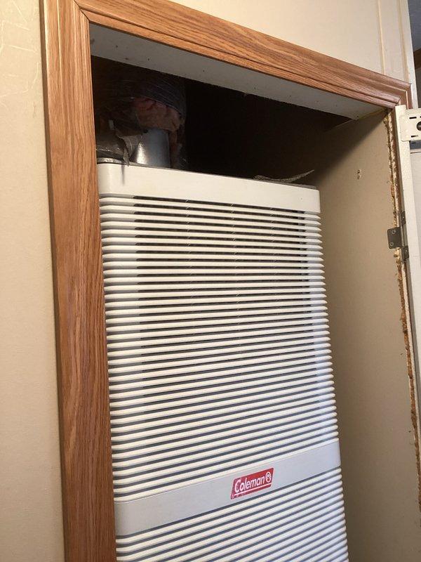 Conducted comprehensive HVAC system evaluation at mobile home residence to provide estimate for complete furnace and air conditioning replacement. Inspected existing Coleman packaged terminal unit installed in wall-mounted wooden cabinet enclosure, documenting current system configuration including electrical control board with blue relay, wire connections, and condensate management components. Currently operational system assessed for replacement specifications, with detailed photographic documentation of existing electrical connections, control box wiring, and through-wall installation parameters to ensure accurate equipment sizing and installation planning for new system.