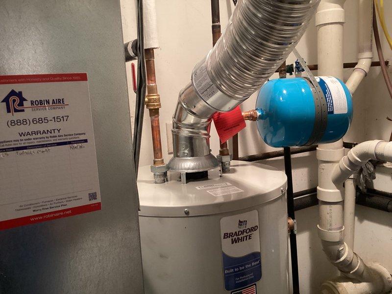 Completed installation of a 40-gallon Bradford White tanked water heater in residential utility space. Installation included proper venting with metallic flexible duct, connection of hot and cold water supply lines with copper piping, installation of expansion tank with appropriate fittings, and integration of necessary shut-off valves and pressure relief components. All plumbing connections were secured and tested for proper operation, with the unit fully operational upon completion.