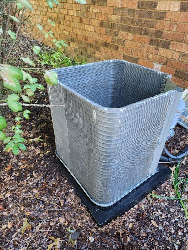 Completed scheduled air conditioning maintenance on residential split system. Inspected outdoor condenser unit positioned on mounting pad against brick exterior, confirmed proper installation and clearances. Documented condenser unit condition with exterior showing normal wear patterns and adequate airflow access through louvered panels. Inspected condensate drain pan assembly, noting standing water present in collection tray with drain pump mechanism and mounting plate visible. All electrical connections to drain pump components observed and documented. Unit operational at time of inspection.