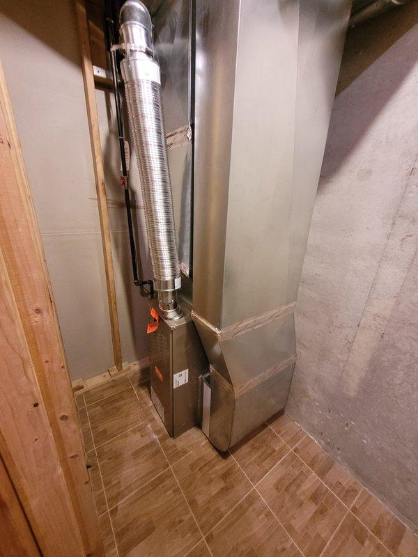 Successfully installed a new Bryant 80% efficiency furnace in the mechanical space. The installation included proper gas line connections with flexible corrugated connectors and threaded fittings, aluminum flex ductwork routing from the unit with secure black strap mounting, and appropriate electrical controls with wall-mounted disconnect switch. Unit was positioned against concrete foundation walls on finished flooring, with all connections properly secured and tested for safe operation.