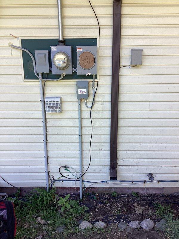 Completed electrical wiring installation for interruptible service at residential property. Installed meter base, service entrance equipment, and associated conduit system on exterior wall with proper grounding and weatherhead connections. All components mounted securely to backing board per code requirements, with conduit runs properly secured and terminated at grade level.