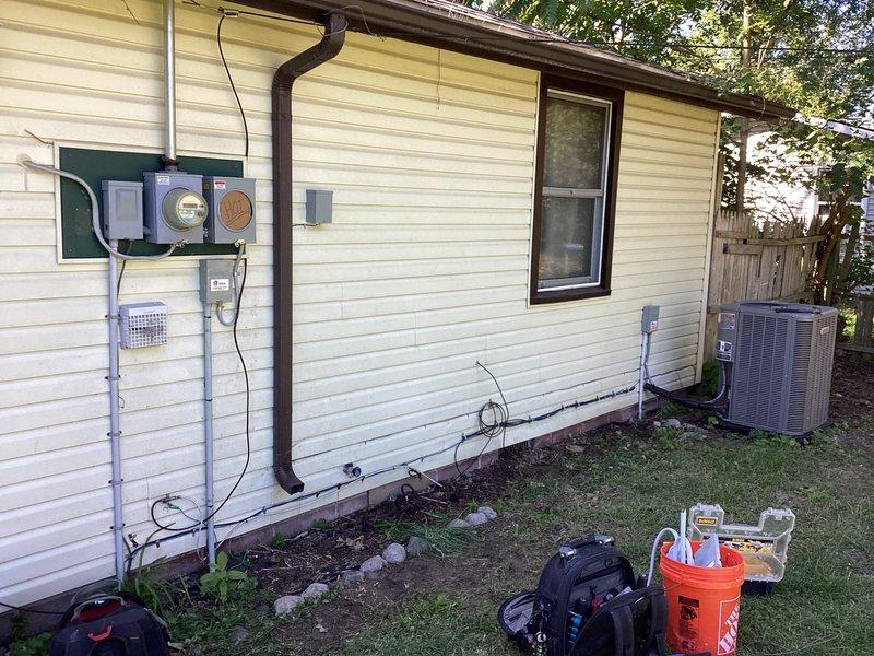 Completed electrical wiring installation for interruptible service at residential property. Installed meter base, service entrance equipment, and associated conduit system on exterior wall with proper grounding and weatherhead connections. All components mounted securely to backing board per code requirements, with conduit runs properly secured and terminated at grade level.