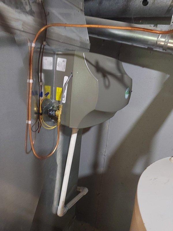 Installed whole-house humidifier unit on existing HVAC ductwork system, including mounting the beige metal humidifier cabinet to wall, running copper water supply line with proper connections, integrating electrical wiring with wire nut terminations, and connecting white PVC drainage line. Verified level installation of unit and ensured all plumbing and electrical connections were secure and properly integrated with the forced-air system.