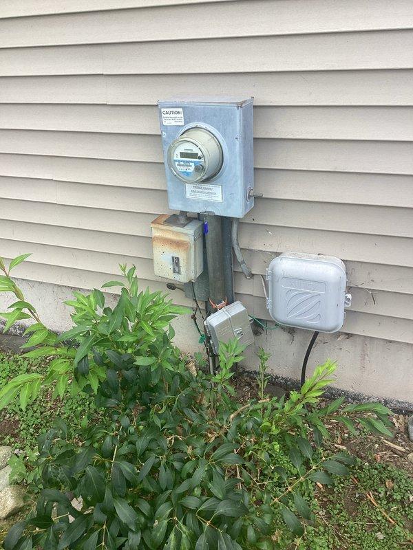 Conducted site assessment for upcoming generator installation scheduled for 9/29. Documented existing electrical infrastructure including main meter assembly, weathered junction box, and conduit routing on exterior wall. Photographed gas meter location and utility connections to verify clearances and placement requirements for generator unit in rear yard. Confirmed site plan requirements and noted installation parameters specifying 2-4 schedule with rigid conduit specifications prior to 2-pole connection point.