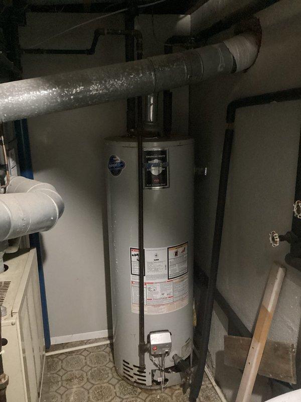 Conducted comprehensive water heater evaluation and assessment of existing HVAC system in residential utility space. Inspected white cylindrical tank-style water heater unit, documenting current installation configuration, plumbing connections, and valve controls. Evaluated beige furnace unit with adjacent ductwork and examined condensate drainage system with white PVC piping. Photographed all mechanical equipment, pipe routing, and system components to support estimate preparation for potential water heater replacement and full system upgrade considerations.
