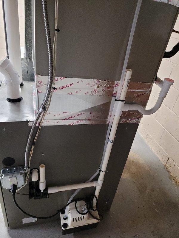 Completed installation of Lennox furnace system in basement utility room, including proper mounting of air handler unit against prepared wall surface. Installed condensate drainage system with white PVC piping routed vertically through interior space and exterior wall, terminating with appropriate elbow fitting on building exterior, and connected condensate pump with dedicated electrical supply to ensure proper moisture removal from system.