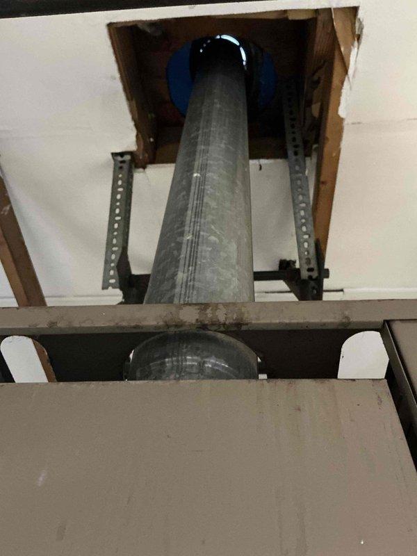 Inspected existing ceiling-mounted HVAC duct system in garage/workshop area. Evaluated rectangular metal air handler attachment points and support infrastructure. Identified potential upgrade opportunity where large cylindrical galvanized duct penetrates ceiling, noting suboptimal sealing and mounting hardware configuration. Recommended replacement of current ductwork with properly sized system including improved ceiling penetration seals and reinforced mounting brackets.