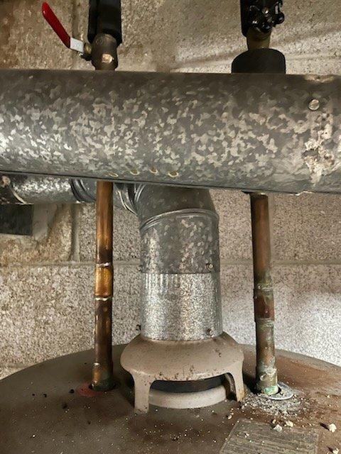 Conducted inspection of dual A.O. Smith water heater system in basement utility area. Units showed signs of aging including oxidation on copper pipes and mineral buildup on components. Evaluated flue pipe connection to ceramic base and checked integrity of red valve handle on left pipe assembly. System appears functional but exhibits normal wear consistent with regular use.