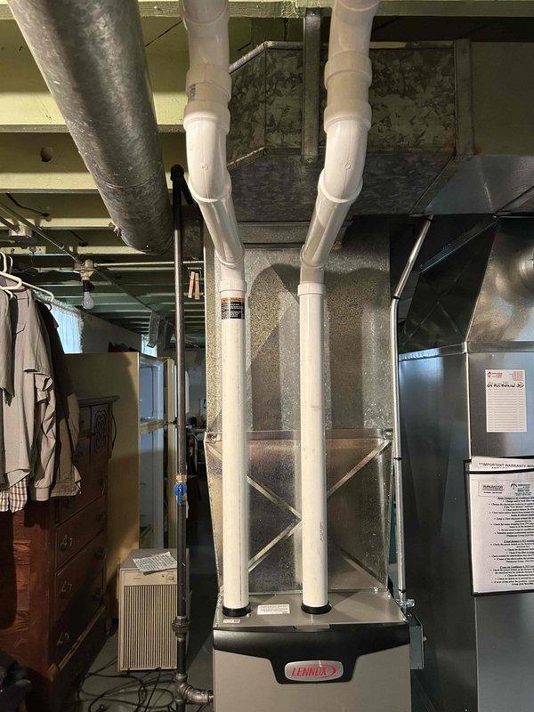 Completed installation of PVC venting system for Lennox furnace unit in basement, including proper routing through exterior siding with appropriate elbow joints and connections. System includes dual intake/exhaust PVC pipes properly secured and connected to the furnace unit, ensuring code-compliant ventilation for safe and efficient operation.