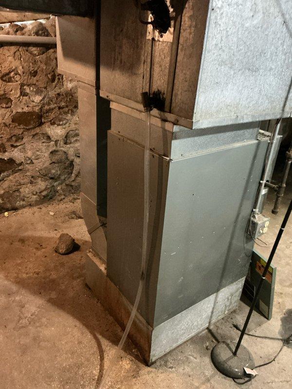 Conducted evaluation of a residential HVAC system requiring replacement due to multiple issues. The outdoor heat pump/AC unit was found severely compromised by excessive snow accumulation blocking proper airflow, potentially causing operating inefficiencies and possible damage. Indoor inspection revealed an aging furnace/air handler installed in an unfinished basement area with suboptimal installation conditions including proximity to bare stonework and unfinished flooring.