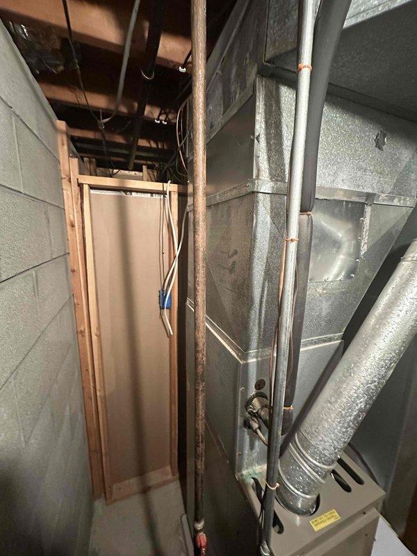 Conducted inspection of residential HVAC system in basement utility area. Existing setup includes furnace/air handler with connected ductwork, alongside water heater with copper piping. System appears functional but evaluation performed for potential replacement options based on age and efficiency considerations.