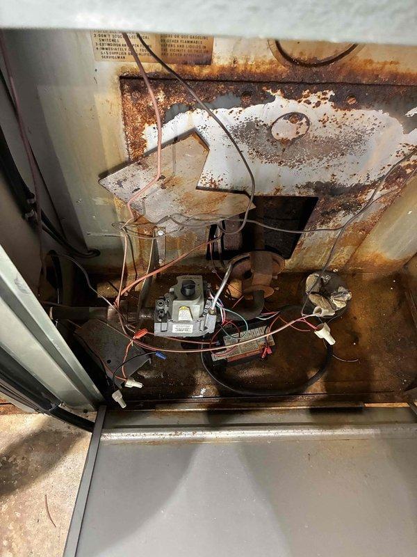 Inspected 10+ year old system with no heat complaint. Discovered severe internal corrosion and rust damage to heat exchanger and major components. Photos documented extensive oxidation on metal surfaces, deteriorated housing with holes, and significant rust accumulation at unit base. Determined heat exchanger has failed completely, creating unsafe operating conditions. Recommended immediate system replacement due to safety concerns and irreparable condition of critical components.