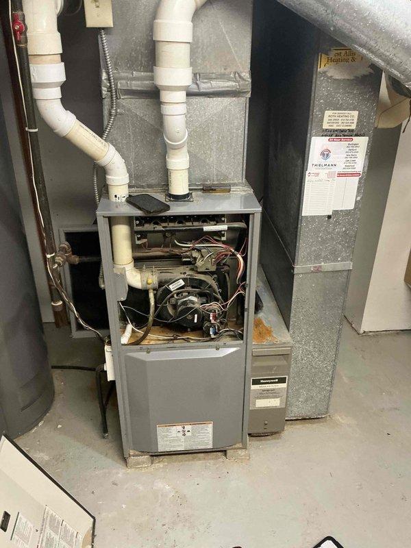 Completed comprehensive inspection and photo documentation of residential HVAC system located in basement utility area. System consists of a gas furnace with connected PVC ventilation/drainage pipes, blower assembly, control board, and metallic ductwork. Front access panel was removed to inspect internal components, revealing normal operational condition of electrical wiring and mechanical elements.