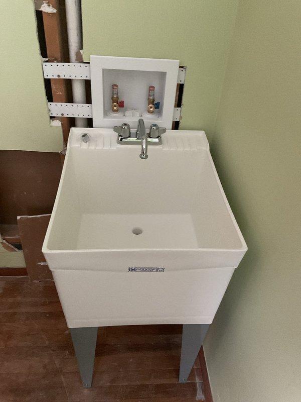 Completed installation of a utility sink with chrome faucet in customer's space, connecting supply lines to existing hot and cold water valves. Verified proper seating of sink on metal legs and ensured access panel remains functional for future maintenance needs.