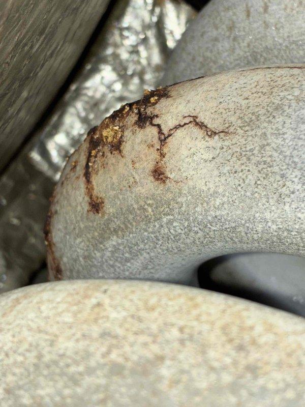 Performed scheduled tune-up on aging HVAC system located in confined utility area. Observed significant rust and water damage on unit components including visible corrosion on piping and metal ducting. Documented deterioration with photos for record, particularly noting stress lines and potential cracking that may require future attention.