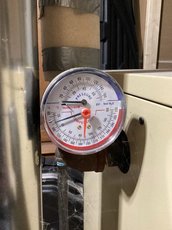 Inspected client's boiler system, noting pressure and temperature within acceptable range on Honeywell gauge. Evaluated exposed ductwork and associated red valve/control mechanism in partially finished mechanical area. System appears functional with minor surface discoloration on ductwork requiring no immediate attention.