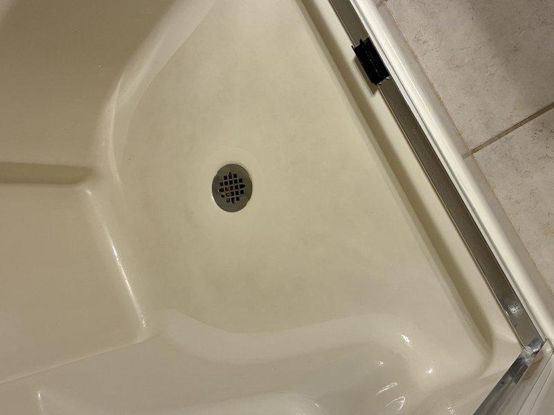 Conducted inspection of shower system with focus on drainage components. Accessed wall cavity to examine plumbing infrastructure, revealing PVC drain pipe with elbow joint surrounded by insulation. Verified shower base integrity and confirmed proper slope toward drain without signs of damage or leakage.