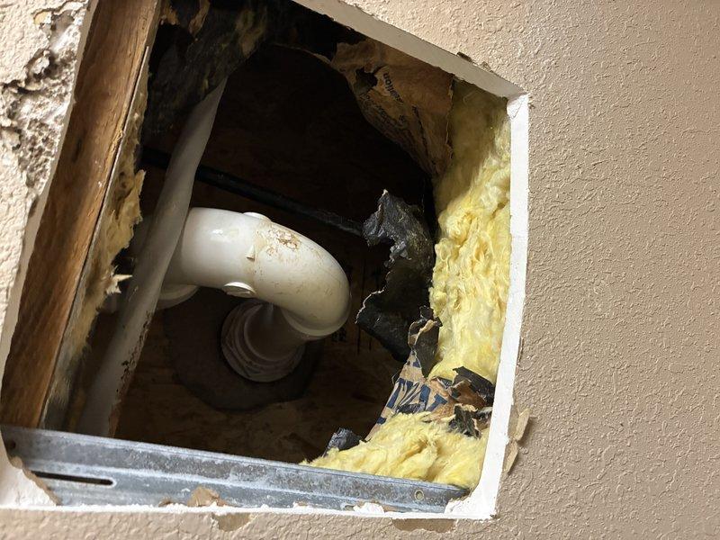 Conducted inspection of shower system with focus on drainage components. Accessed wall cavity to examine plumbing infrastructure, revealing PVC drain pipe with elbow joint surrounded by insulation. Verified shower base integrity and confirmed proper slope toward drain without signs of damage or leakage.