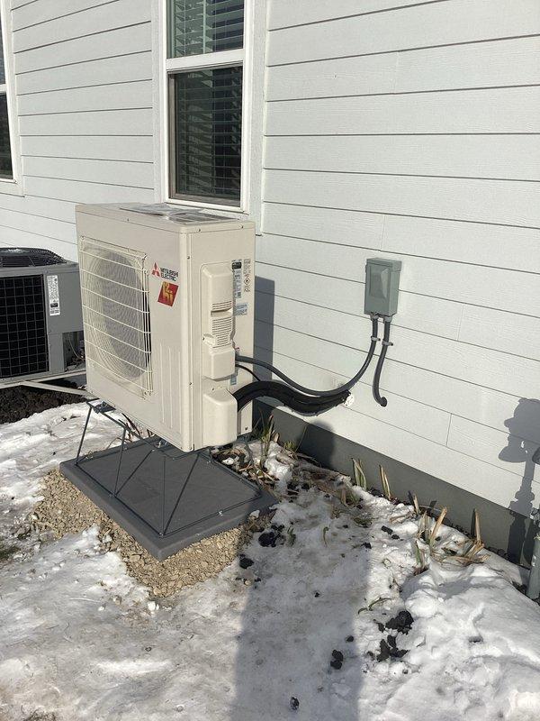 Completed installation of a Mitsubishi mini-split heat pump system featuring outdoor condensing unit properly mounted on a concrete pad adjacent to customer's residence. Connected all refrigerant lines with proper insulation and installed electrical disconnect box on exterior wall according to manufacturer specifications and local codes.